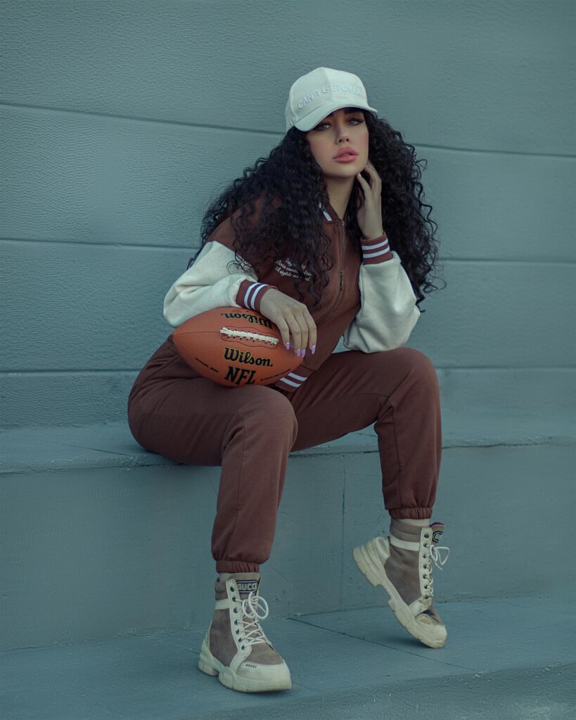 Fashion-forward woman poses with an American football, showcasing sporty street style.